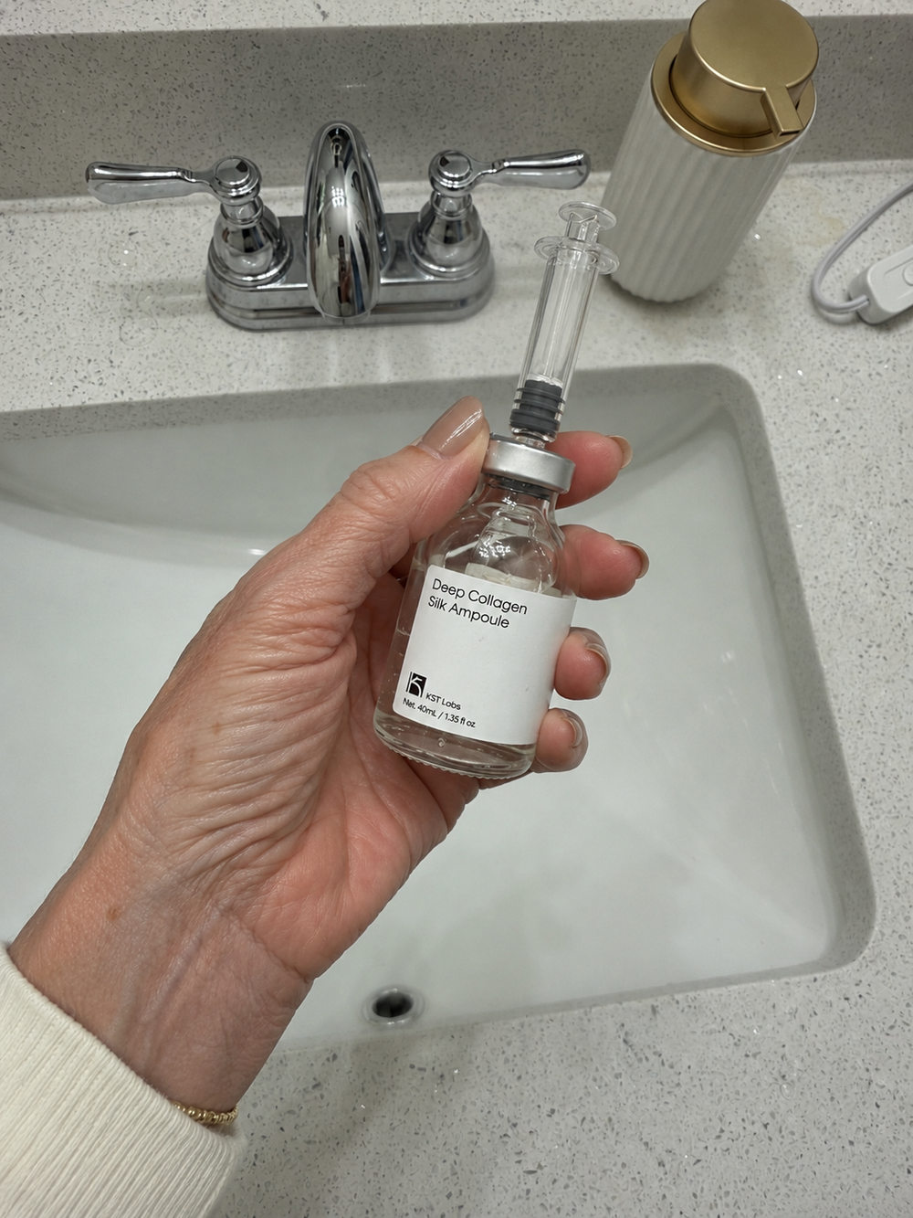 A woman's hand setting the ampoule vial down on a ceramic counter, not picking it up.